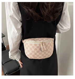 Detail of a beige half-moon waist bag with repeating white M patterns and dual zippers
