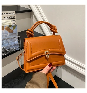 Detail of caramel leather handbag featuring twisted handles and gold U-shaped metal lock