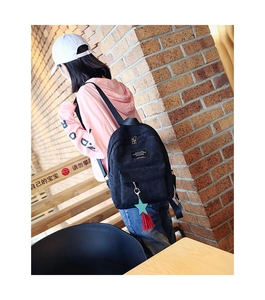 Detail of a black corduroy backpack with a red tassel charm and casual patch logo