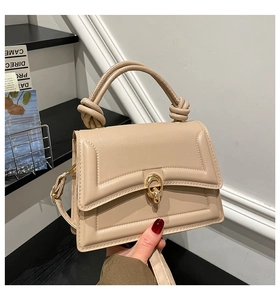 Close-up of beige leather handbag featuring a golden oval twist lock and knotted handle