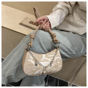 Detail of cream shoulder bag featuring white abstract lettering and silver chain with heart charm