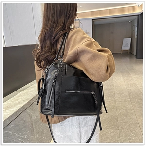 Close-up of a large black soft leather tote bag with functional zippers and glossy finish