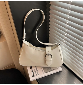 Detail of a creamy white crescent baguette bag with polished silver buckle decoration