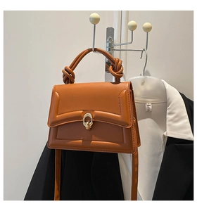 Close-up of brown leather bag featuring a chunky knotted handle and golden ring metal clasp