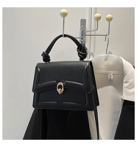 Detail of black leather square bag showing the gold metal oval buckle and knotted handle