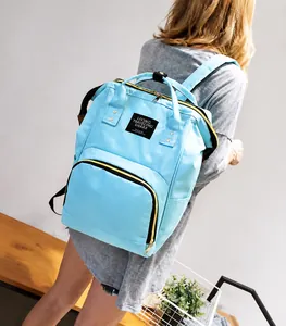 Rear view of a light blue oxford fabric travel backpack worn by a model in an indoor setting