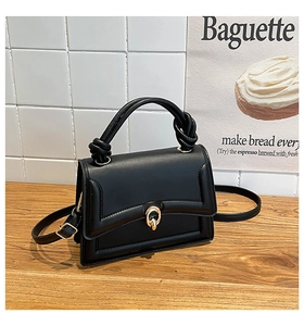Close-up of black leather handbag with golden round lock and twisted top handle design