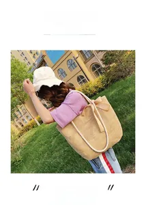 Detail view of woven straw tote bag featuring white rope handles and a brown satin bow