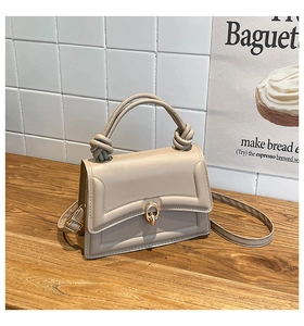 Detailed close-up of beige handbag with gold ring buckle and twisted handle design