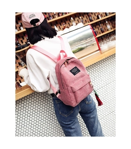 Detailed close-up of pink corduroy backpack with zipper pocket and red tassel pendant