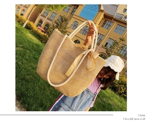 Detail of a large woven straw tote bag featuring white cotton rope handles and satin bows