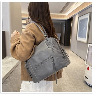 Detail of grey soft leather tote bag with zipper pocket and woven tassel charm detail