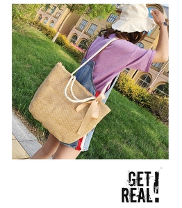 Detail of woven straw tote bag with cotton rope handles and a brown satin ribbon bow