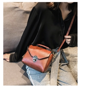 Borsa a tracolla in pelle marrone con chiusura a scatto indossata da modella in interni