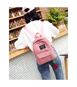 Detailed view of pink corduroy mini backpack with colorful ribbon charm and woven label