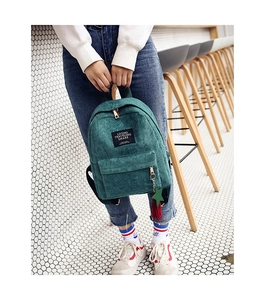 Detail of green corduroy backpack featuring a black woven label and star fringe charms