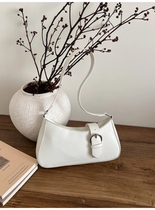 Detail of white leather baguette bag featuring a silver circular buckle and minimalist strap