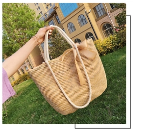Detail of woven straw tote bag featuring thick cotton rope handles and a satin bow knot
