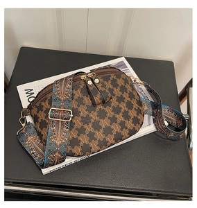 Detail view of double zippers and vintage M-print pattern on a brown crossbody bag
