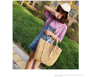 Detail of a beige woven straw beach bag featuring a light khaki ribbon bow and cotton handles