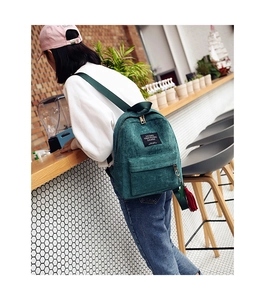 Detail of dark green corduroy backpack showing textured fabric and red tassel accessory