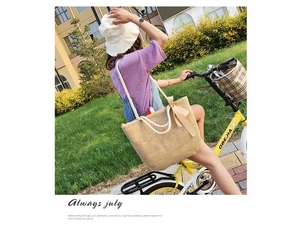 Outdoor shot of a beige woven straw tote bag with a ribbon bow on a yellow bicycle