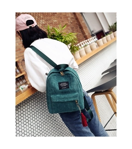 Detail view of turquoise corduroy backpack with metal zipper and red tassel on shoulder