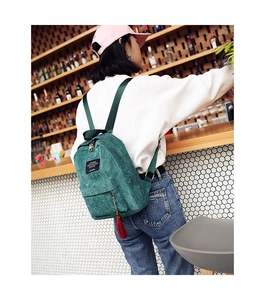Detail of dark green corduroy backpack with red tassel and square label on bar background