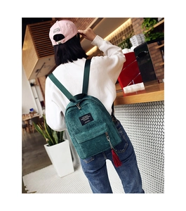 Detail of green corduroy backpack with red tassel charm and living traveling share label