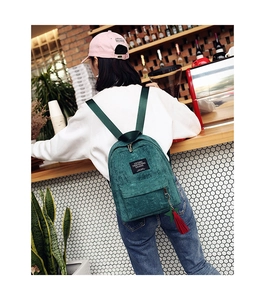 Deep green corduroy backpack for women shown in use with stylish red tassel detail