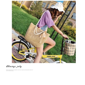 Close-up of woven straw tote bag with rope handles and bow on a bicycle basket