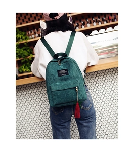 Dark green corduroy backpack featuring red tassel keychain and black label in a cafe setting