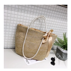Close-up of woven straw tote bag featuring a large satin bow and thick rope handles