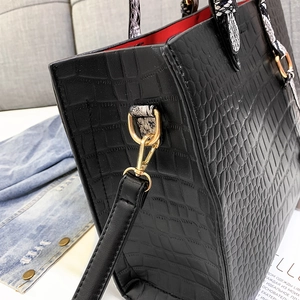 Detail of black faux crocodile tote bag showing red lining and gold hardware clip