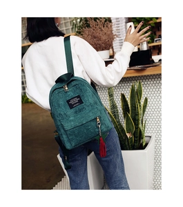 Dark green corduroy backpack with stylish star charm tassel shown in a cafe setting