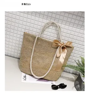 Detail of straw woven tote bag featuring white cotton handles and a champagne satin bow