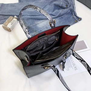 Detailed view of crocodile pattern tote bag featuring red lining and snake print handles