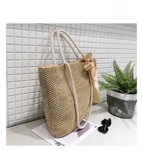 Detail of straw woven tote bag featuring white cotton rope handles and silk bow decoration