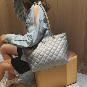 Quilted silver tote bag with golden chain strap and deer charm shown by female model