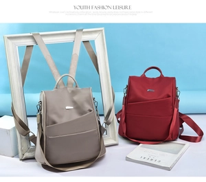 Detail view of khaki and wine red nylon backpacks with metallic trim and side pockets