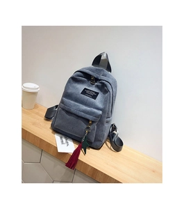 Detail of grey-blue corduroy backpack featuring colorful tassel charms and textile logo