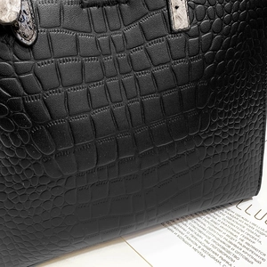 Detailed close-up of black crocodile embossed leather handbag with snakeskin handle detail