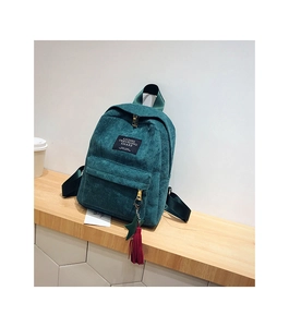 Detail of green corduroy backpack showing zipper pocket, star charm, and logo patch