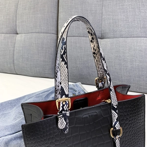 Detail of black crocodile-embossed tote bag featuring snakeskin handles and red inner lining