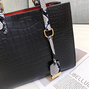 Detail of black crocodile-embossed tote bag featuring snakeskin handles and red lining