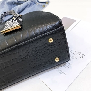 Detail of black crocodile-embossed handbag featuring gold studs and faux snake strap accessory