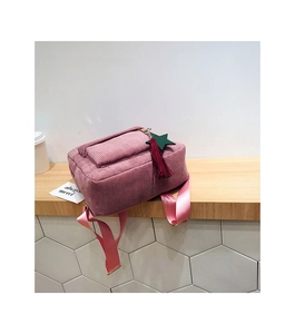 Pink corduroy backpack with decorative star and tassel charms on a wooden shelf