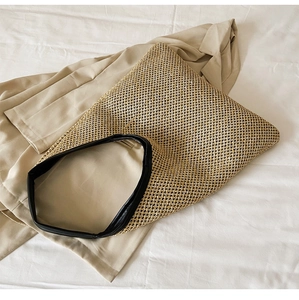 Top view of a woven straw beach tote with black leather trim on a beige blazer background