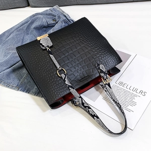 Detail of black crocodile texture handbag with snake print strap and red interior lining