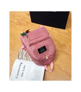 Detail of pink corduroy backpack with black label and green star charm on wood background